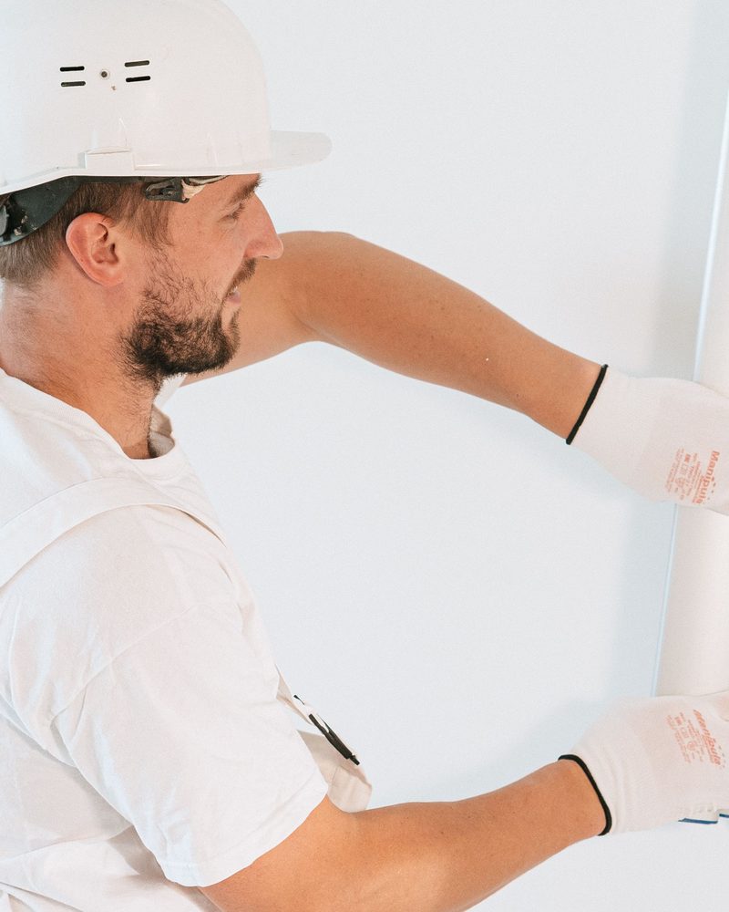 A worker in a hard hat smoothing a white wall with a wide finishing blade