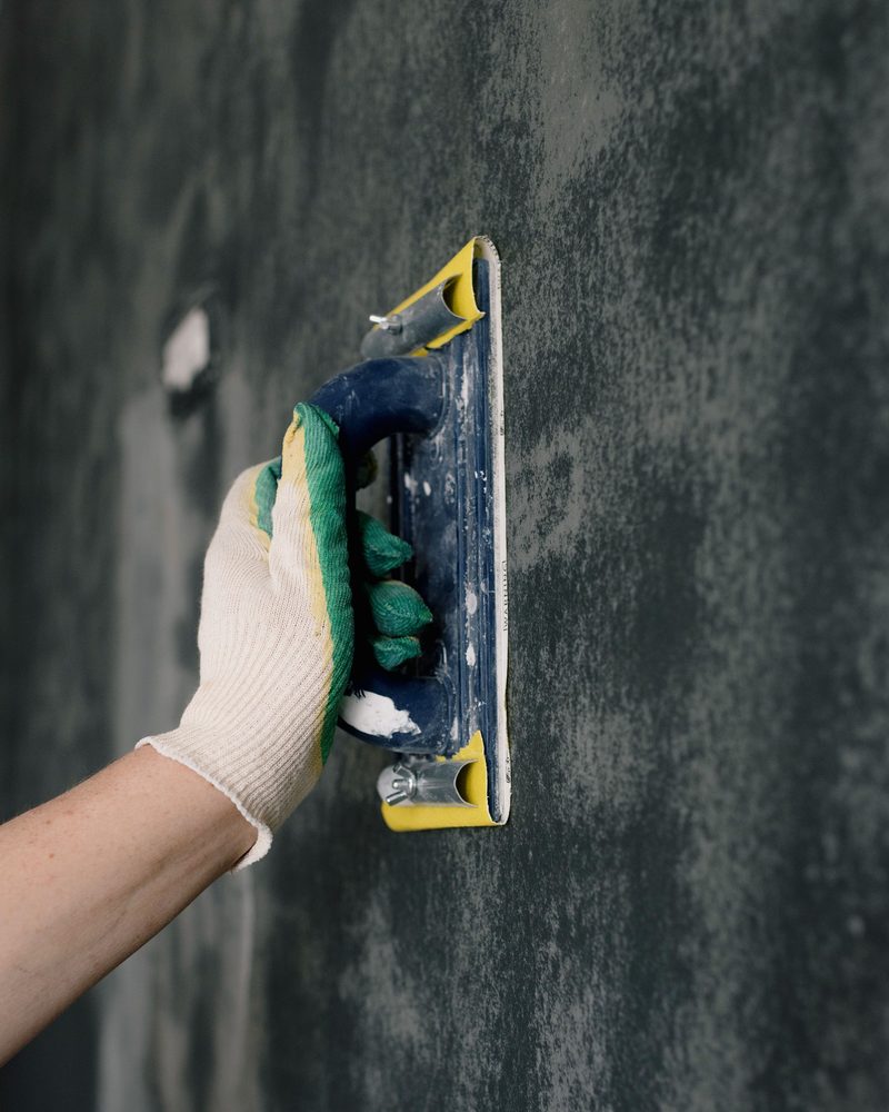 A gloved hand sanding a wall with a hand sanding block